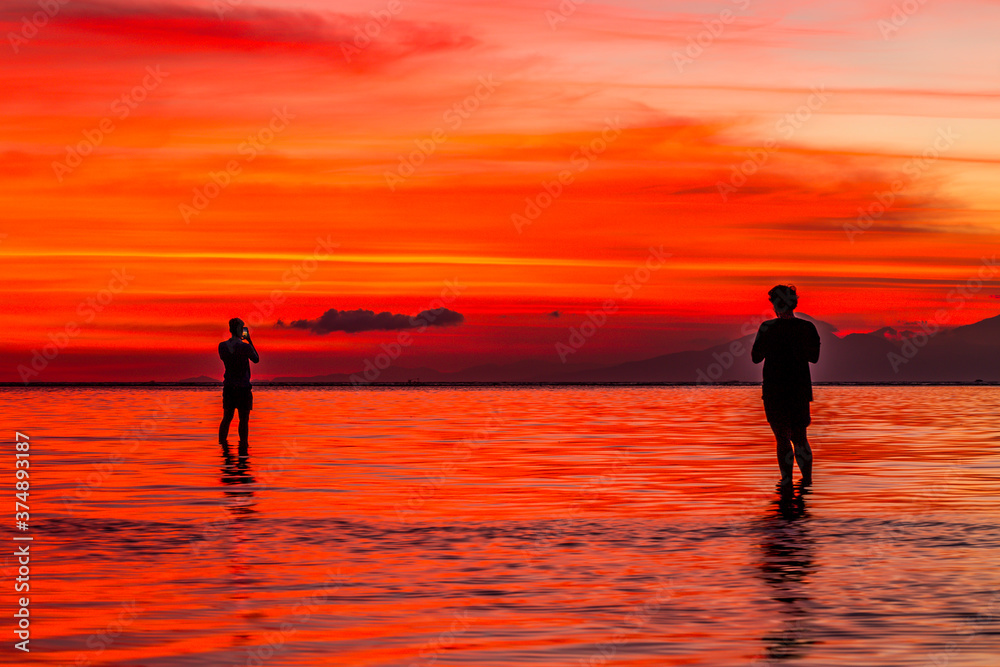 Two people silhouetted against a vivid sunset over the water