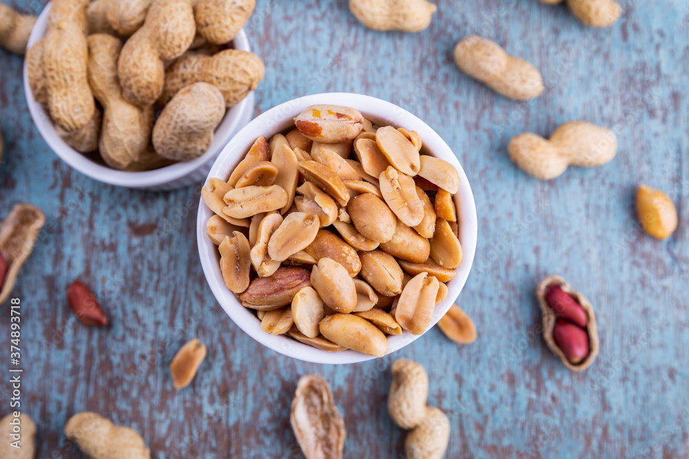Peanuts in a white bowl rests on an old wooden table. Peanuts in a white bowl rests on an old wooden table.