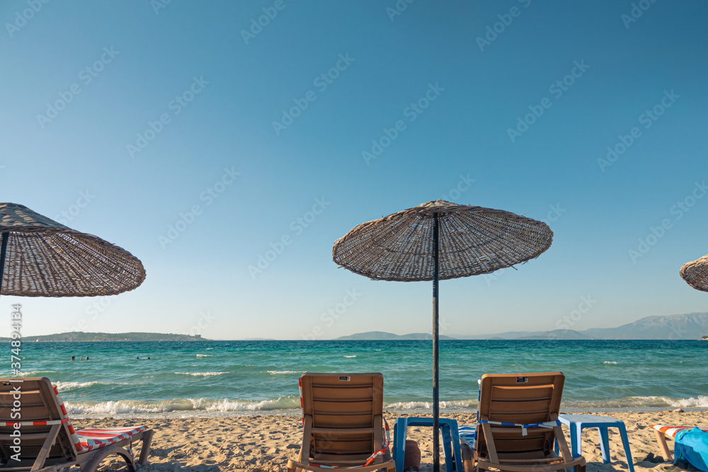 sand beach in Çeşme with straw umbrellas and chaise-longue chairs  as very nice background.