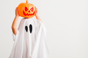 Funny Halloween Kid Concept, little cute child with white dressed costume halloween ghost scary he holding orange pumpkin ghost on hand, studio shot isolated on white background