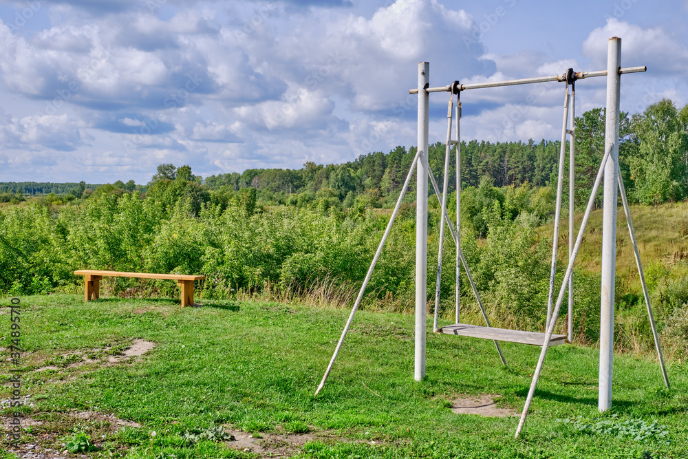 An orange wooden bench stands on a hill over the background of a forest and a beautiful cloudy sky. An orange wooden bench stands on a hill over the background of a forest and a beautiful cloudy sky.
