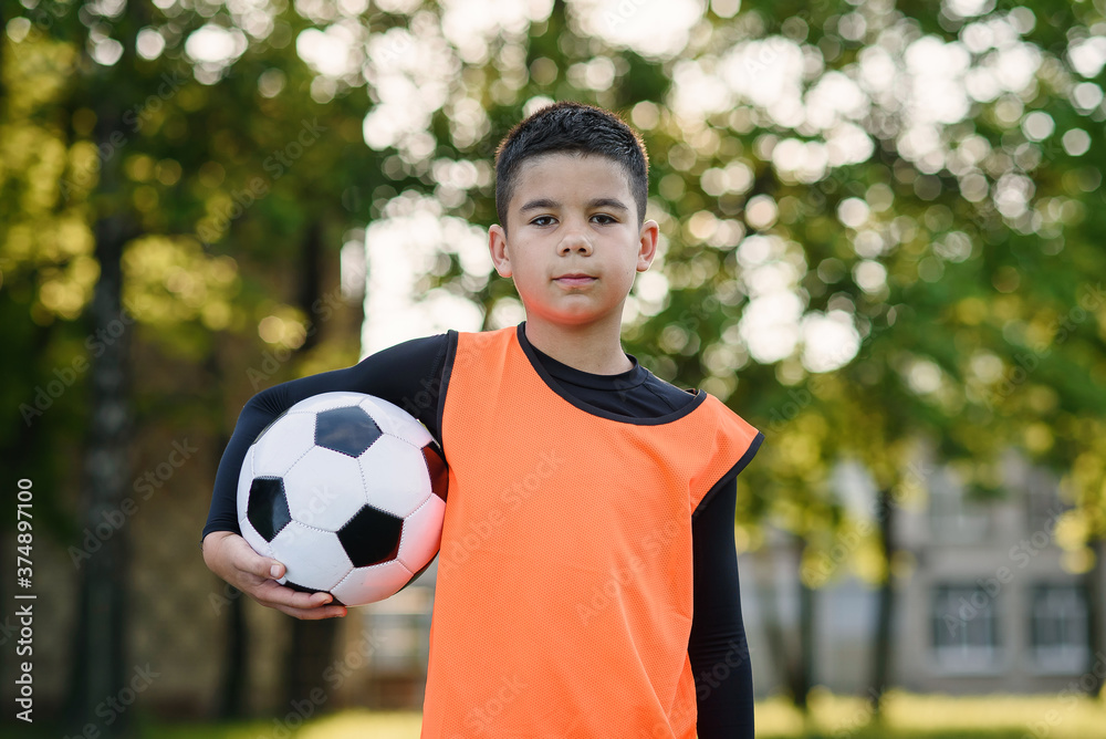 Happy teen boy in football uniform holds a ball after morning training on the stadium at urban green park. Happy teen boy in football uniform holds a ball after morning training on the stadium at urban green park.