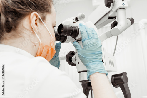 Young woman dentist at her workplace. The doctor uses disposable gloves, a mask and a hat. The dentist works in the patient's mouth, uses a professional tool.