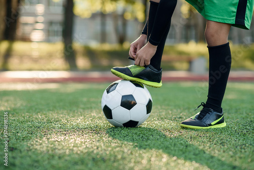 Close up boot of football player which puts his leg on ball and tying shoelace on soccer stadium on the training.