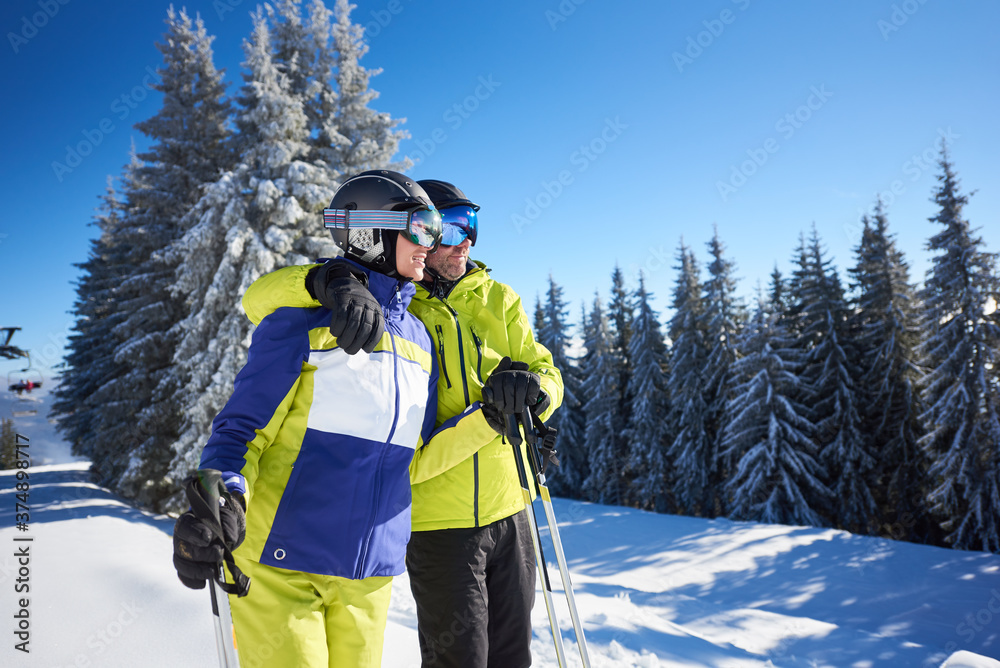 Skiers lifting on top of slope. Cropped view of happy couple embracing and enjoying winter views and mountain scenery. Family vacation, spending time together, winter activities, ski resort concept.