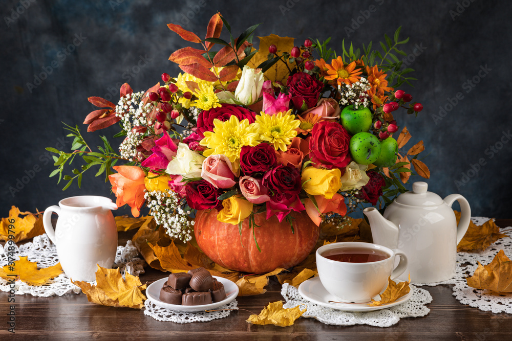 Fototapeta premium Autumn still life with pumpkins, flowers, fruits and yellow leaves on wooden background. Tea and candy