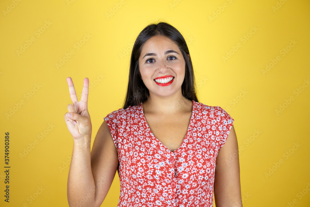 Young beautiful woman over isolated yellow background showing and pointing up with fingers number two while smiling confident and happy Young beautiful woman over isolated yellow background showing and pointing up with fingers number two while smiling confident and happy