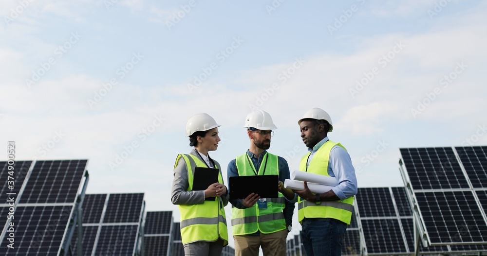 Portrait of electrician engineers in safety helmet and uniform checking solar panels. Group of three engineers at solar station. Portrait of electrician engineers in safety helmet and uniform checking solar panels. Group of three engineers at solar station.