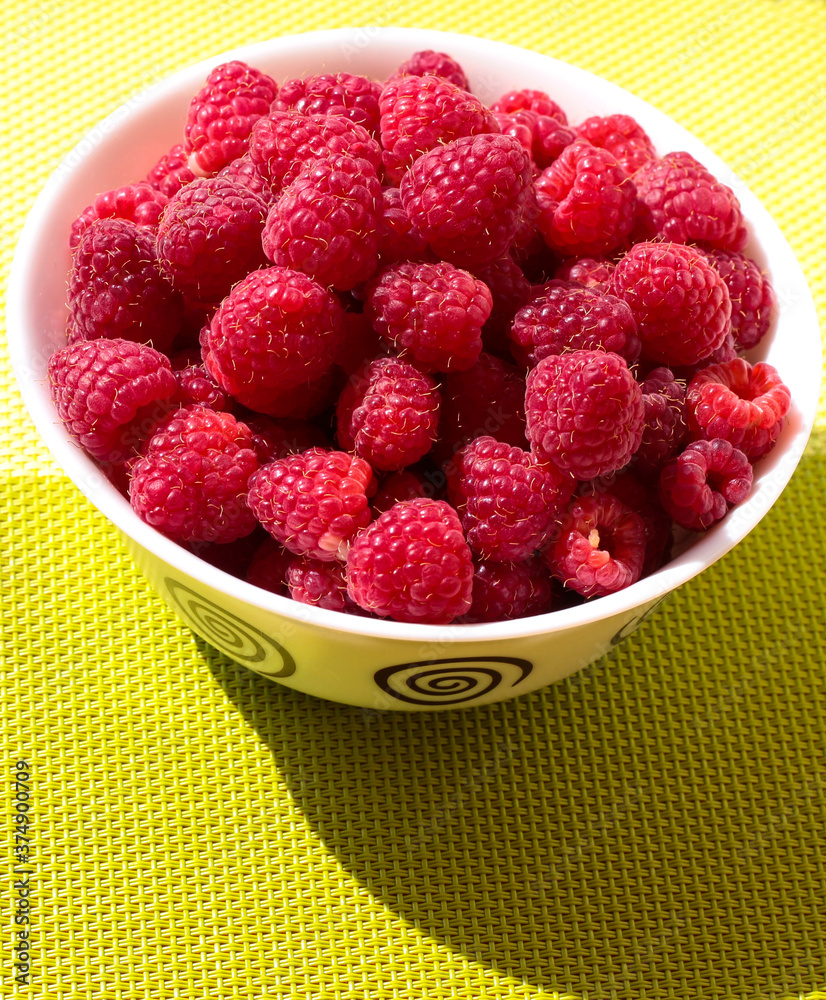 Raspberries in a white plate on a bright background.