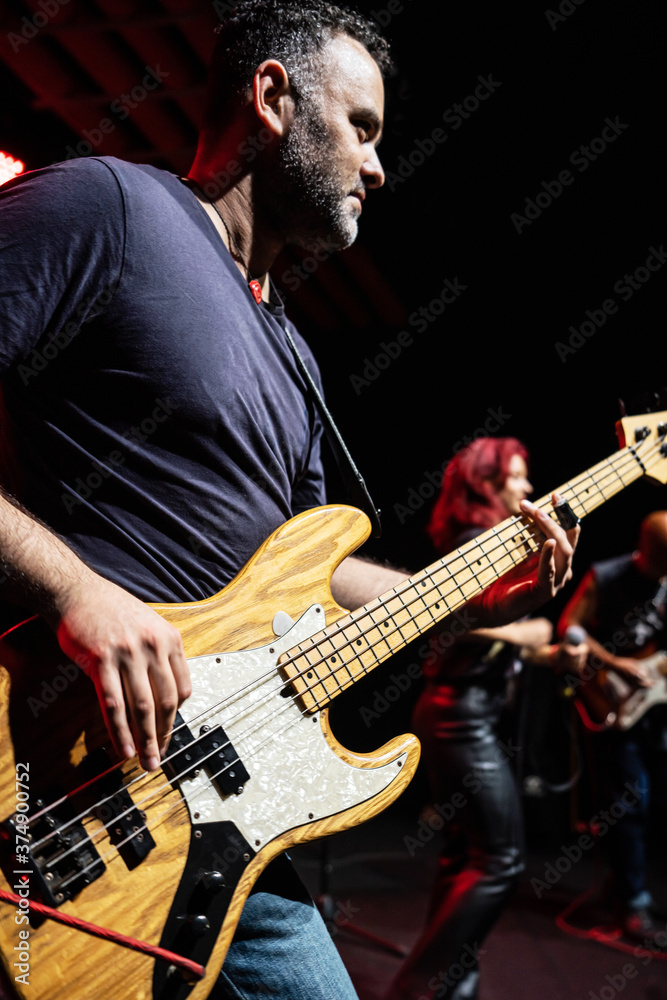 Obraz premium Caucasian Man is Performing on the Stage with Band. Handsome Male Person is Playing on Bass Guitar at Concert.