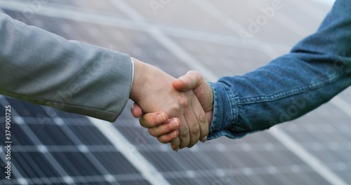 Close up view of shaking hands after discussion on background of photovoltaic solar panels.