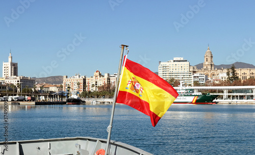 Malaga, Spain: Spanish flag waving in front of the skyline of the old town and the central harbour on a bright winters day