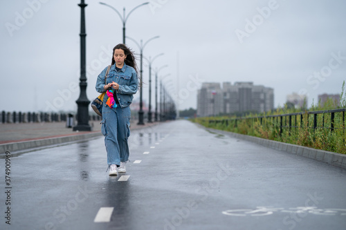 A teenage girl walks on the wet asphalt after the rain with a bright umbrella in her hands. Bicycle way. Street photography. Healthy lifestyle.