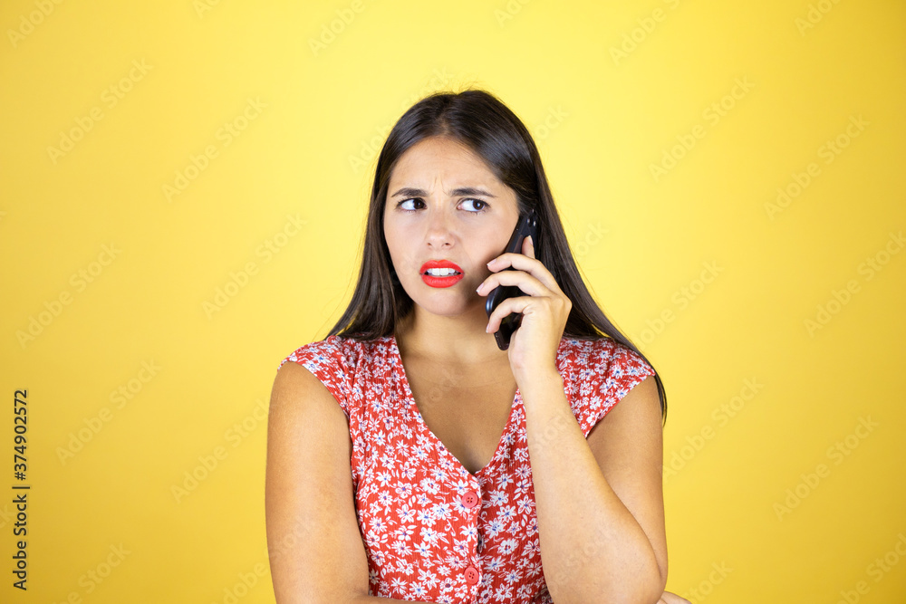 Fototapeta premium Young beautiful woman over isolated yellow background talking on the phone with a confused expression