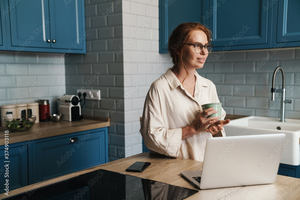 Image of drinking ginger woman drinking coffee and using laptop Image of drinking ginger woman drinking coffee and using laptop