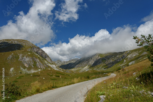 path in the valley, between the mountain peaks of the Alps, between the grass, ascending path to the cloudy mountains