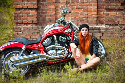 Portrait of charming young woman with red hair near a motorcycle