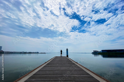 In the background of blue sky and white clouds, the back of a beautiful woman on the plank road on the lake surface