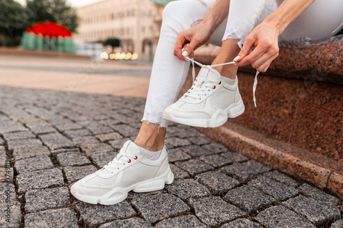 Fashionable girl in stylish jeans sits and ties the laces on the sneakers. photo