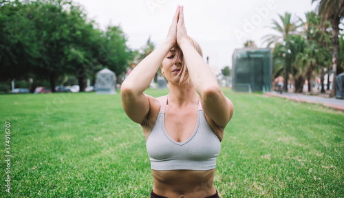 Yoga in nature park performed by attractive young girl dressed in sport top, spiritual training on green grass by calm female in recreation pose meditating searching chakra zen enlightenment