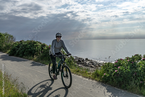 Young woman cyclist riding bicycle along the coastm, Baltic Sea photo