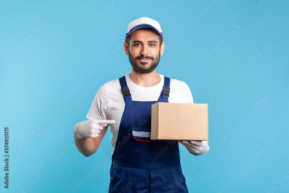 Cargo transportation, delivery service. Friendly worker in uniform pointing at cardboard box and smiling to camera. Courier carrying parcel. Online express shipping, relocation service. isolated Cargo transportation, delivery service. Friendly worker in uniform pointing at cardboard box and smiling to camera. Courier carrying parcel. Online express shipping, relocation service. isolated