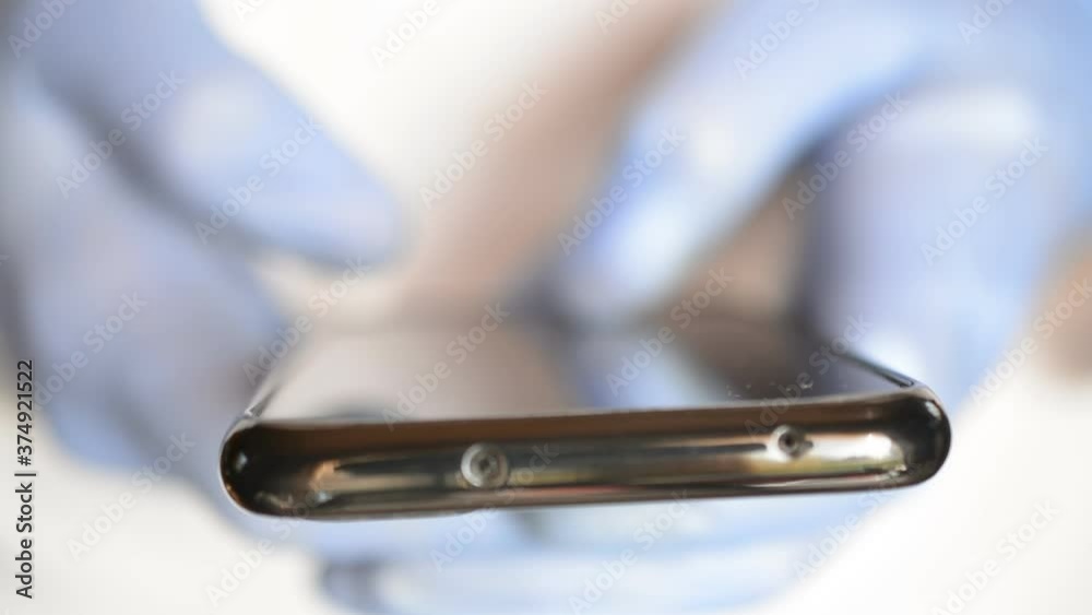 doctor's hands in blue gloves typing message on black phone doctor's hands in blue gloves typing message on black phone