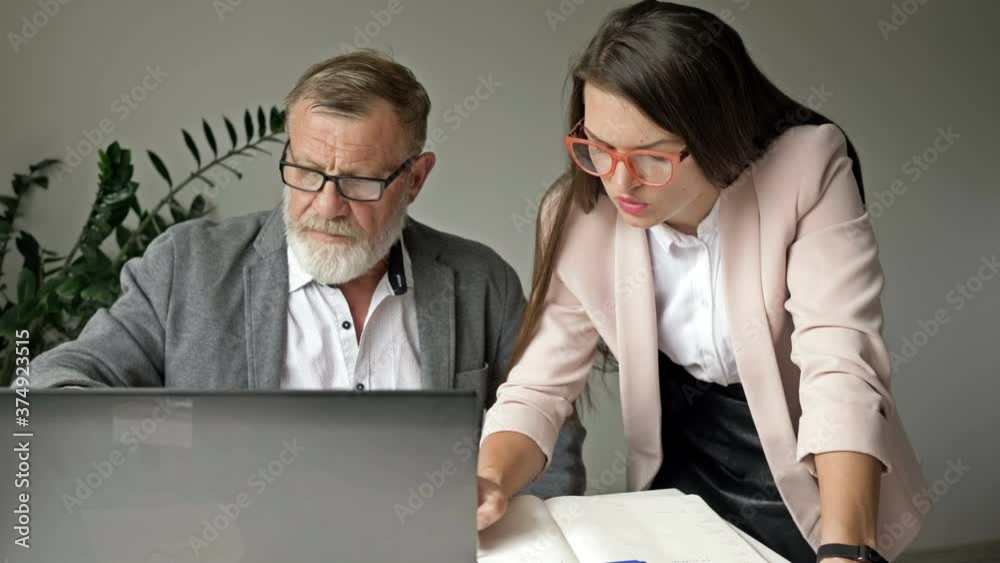 Two business partners work together in the office. Senior man discussing work with her young female colleague. Two business partners work together in the office. Senior man discussing work with her young female colleague.