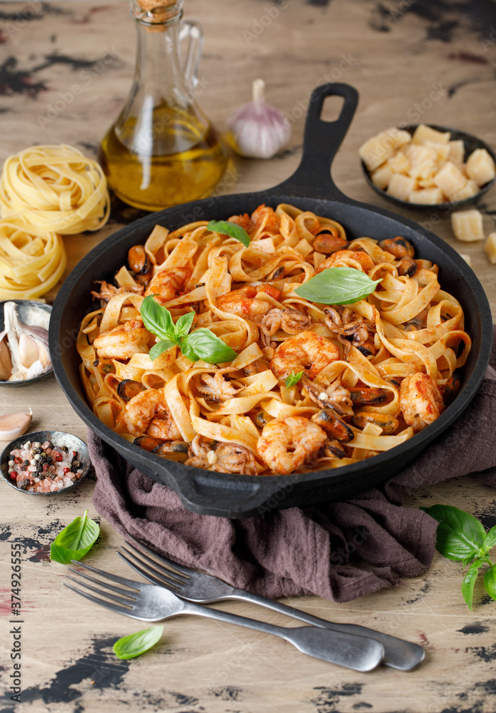 Italian fettuccine pasta with seafood. Seafood pasta with mussels, shrimp and octopus with basil in a cast iron pan Italian fettuccine pasta with seafood. Seafood pasta with mussels, shrimp and octopus with basil in a cast iron pan