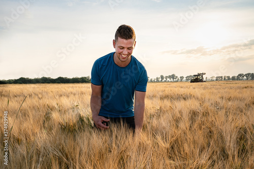 Ackerbau - junger, begeisterter Landwirt  steht im Gegenlicht der Abendsonne im goldgelben Getreidefeld. 