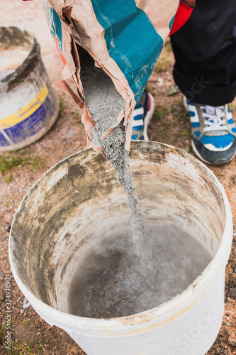 A master bricklayer pours cement from a bag into a bucket - mixing cement mortar for masonry