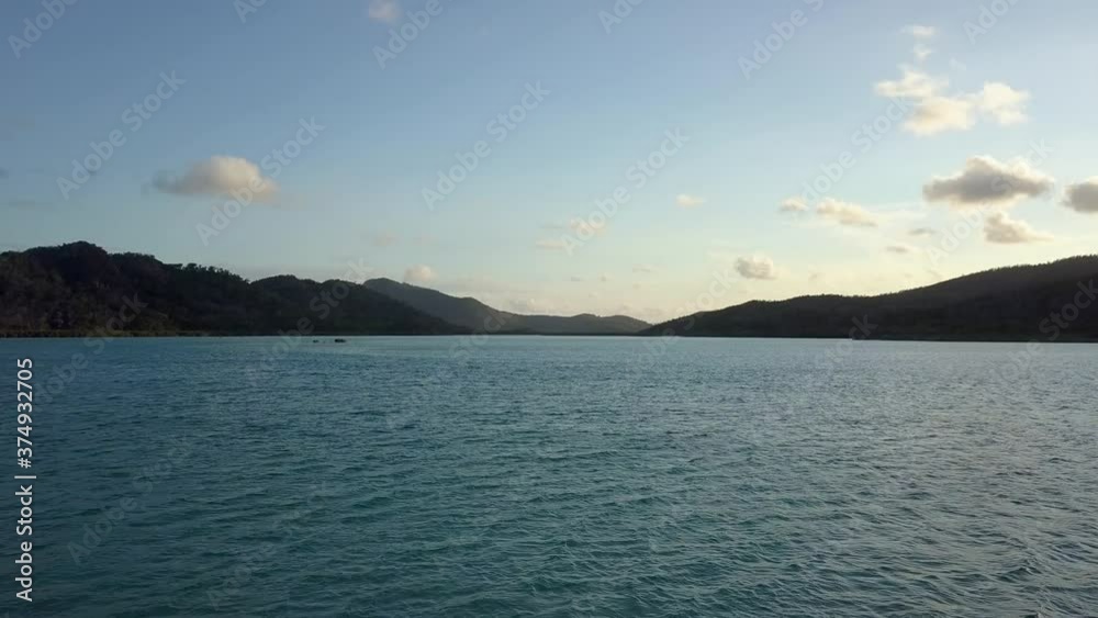 Rising aerial shot over the surface of a calm river and revealing the channel and small mountains in the background Rising aerial shot over the surface of a calm river and revealing the channel and small mountains in the background