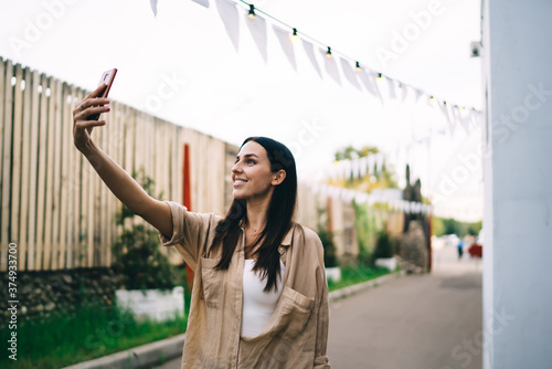 Smiling young lady taking selfie on smartphone on street