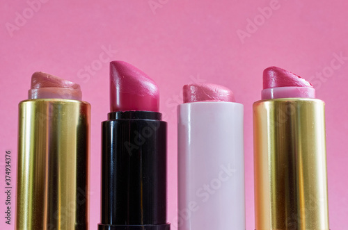 Four old used lipstick tubes stand on a pink background