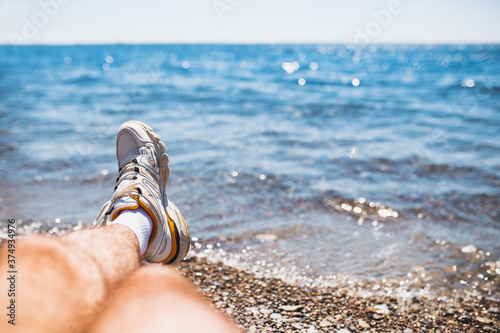 A man sat down on the seashore to rest - a view of the sea horizon - a view of legs in sneakers from the first person photo