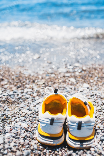 Vertical shot - a pair of white sneakers against the background of the sea - the man took off his shoes and went barefoot giving his feet fresh air