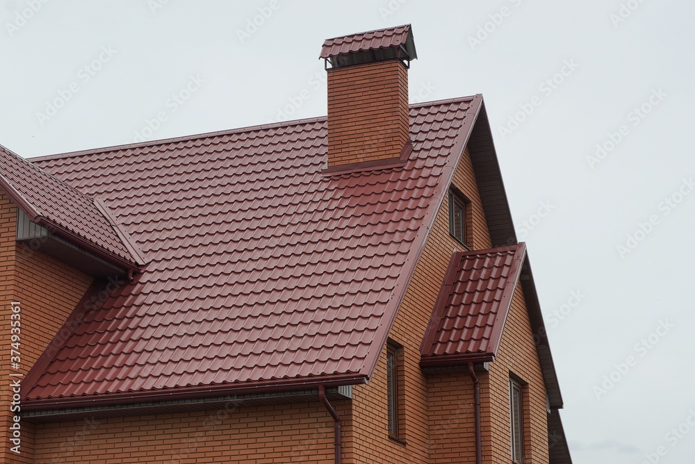 part of the house with red tiles on the roof with  a brick pipe against the  gray sky