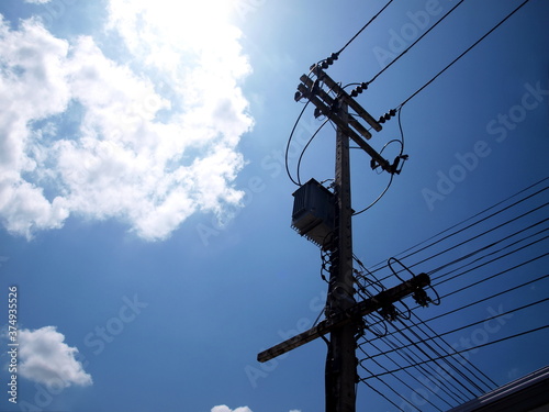 Silhouette of a transformer with wires on a pole.For converting high voltage to low voltage. On a blue sky background there are white clouds reflecting the sunlight with a copy space. Selective focus