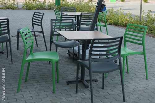 green and black plastic chairs by the table stand on a gray sidewalk outside