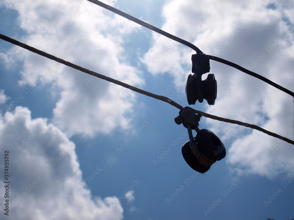 Silhouette of insulators. Damaged electrical fuses hang on a potentially dangerous low voltage cable. On the blue sky background there are white clouds. Selective focus Silhouette of insulators. Damaged electrical fuses hang on a potentially dangerous low voltage cable. On the blue sky background there are white clouds. Selective focus