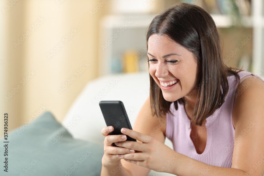 Happy woman using cell phone on a sofa at home Happy woman using cell phone on a sofa at home