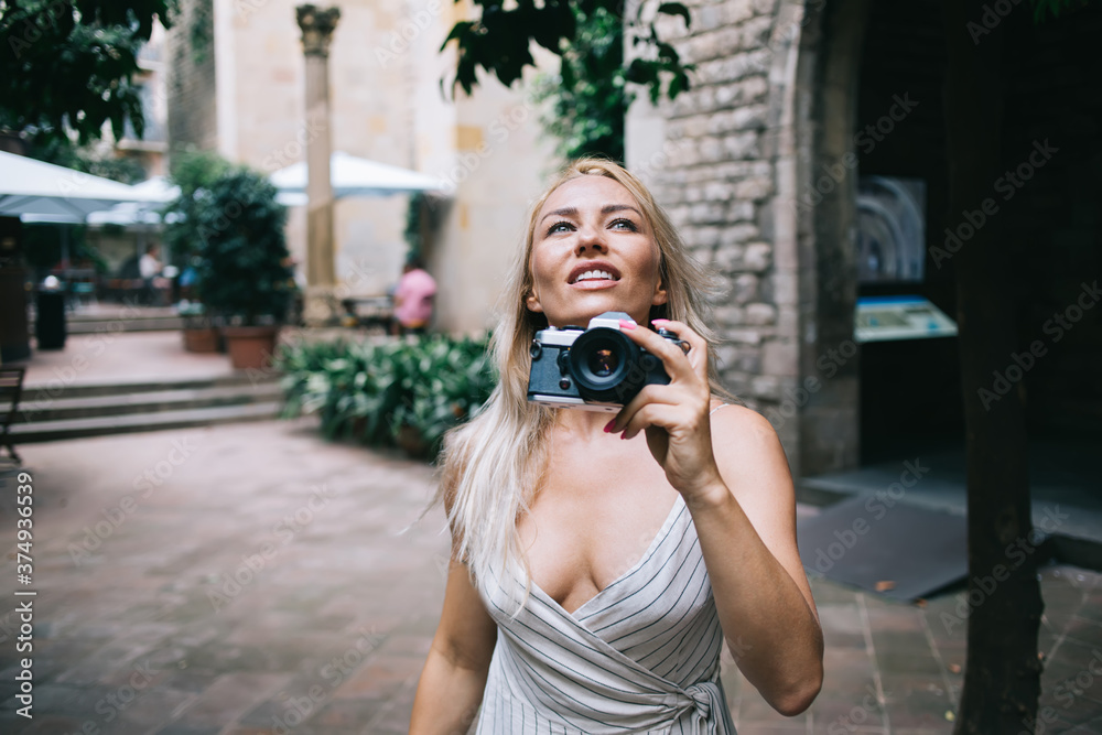 Caucasian woman with retro technology equipment in hand looking up and admire beauty of ancient city enjoying summer international vacations, pretty girl with vintage camera visiting touristic town