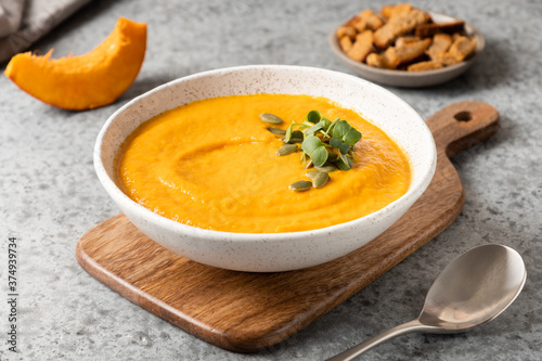 Pumpkin soup with cream garnish microgreens on grey . Close up.