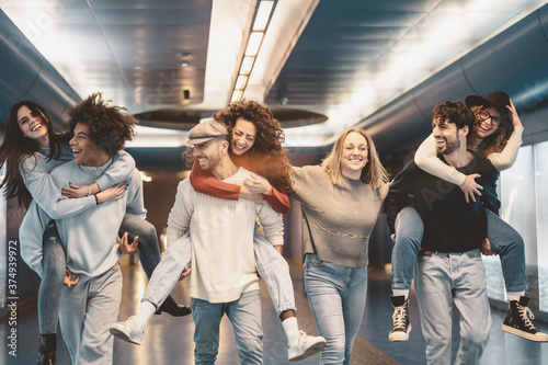 Group young friends having fun piggybacking in underground metropolitan subway - Happy trendy people enjoying nightlife and laughing together - Youth millennial friendship lifestyle concept