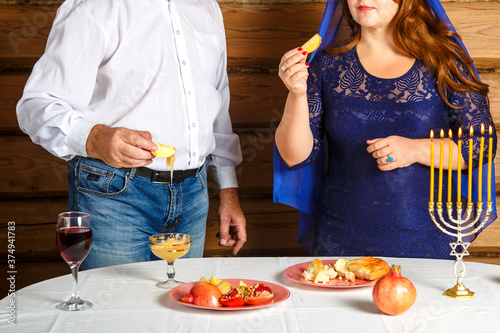 Jewish family, faceless husband and wife in Rosh Ashana at the festive table with burning candles I dip in honey. photo