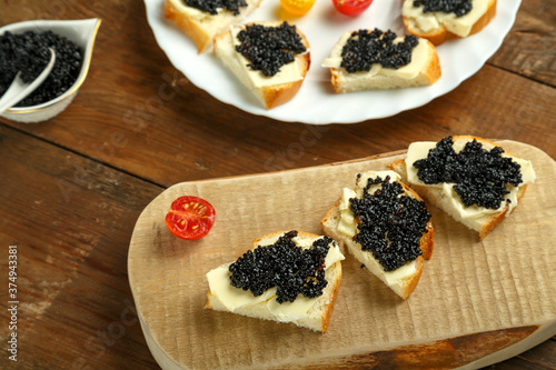 Sandwiches with black caviar on a wooden board on a wooden table next to a caviar dish.