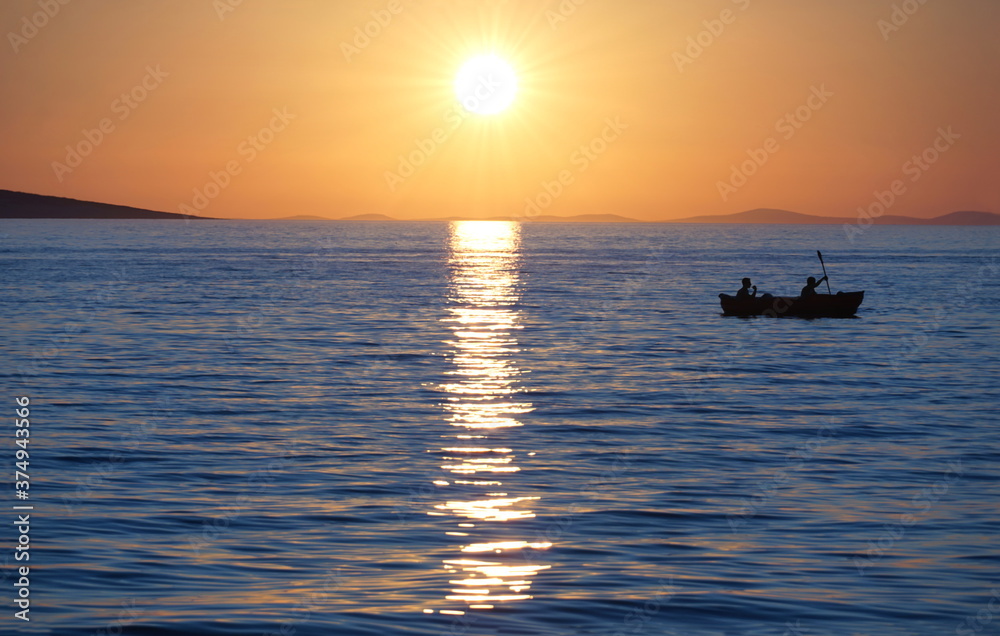 Silhouette of rowers in a small boat on the sea at beautiful sunset