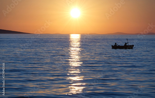 Silhouette of rowers in a small boat on the sea at beautiful sunset © Happy window