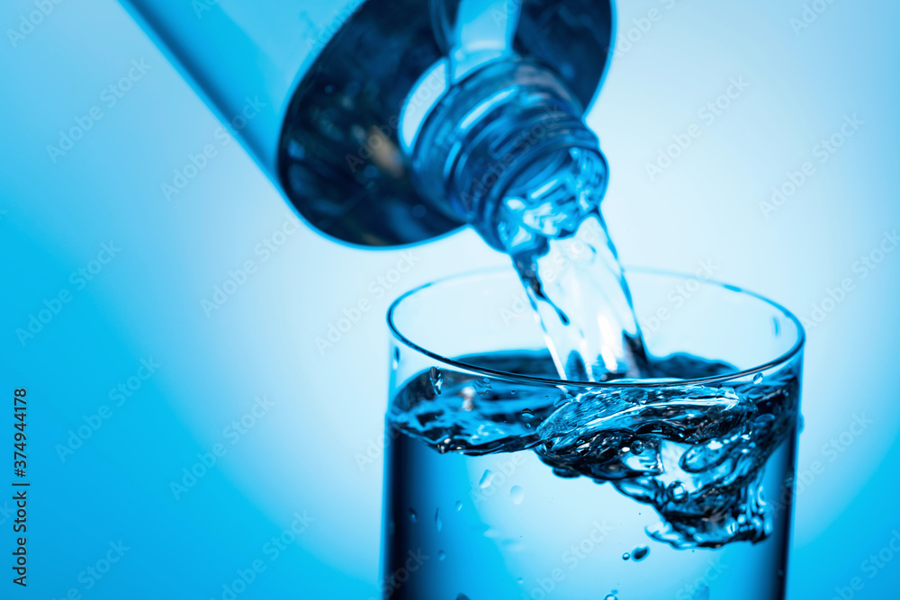 Pouring water from a bottle into glass on a blue background. Pouring water from a bottle into glass on a blue background.