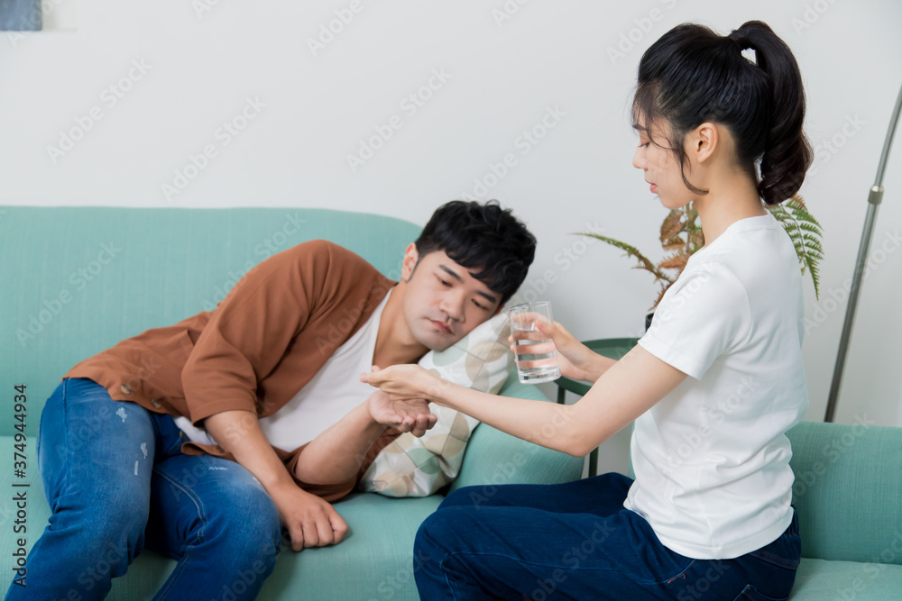 The man feeling uncomfortable. The woman giving medicines and a glass of water to him at home. The man feeling uncomfortable. The woman giving medicines and a glass of water to him at home.